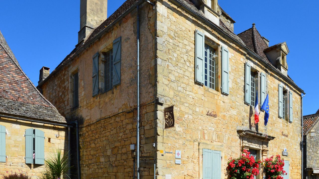 Charming historical French building with stone facade and flags under a clear blue sky.